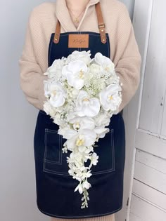 a woman in an apron holding a bouquet of white flowers and greenery on her chest