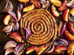 an assortment of vegetables and meats on a baking sheet, including onions, apples, and sausage