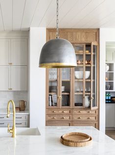 a kitchen with white counter tops and wooden cabinets in the background, along with a large metal pendant light hanging from the ceiling