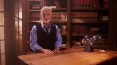 an older man sitting at a table in front of bookshelves