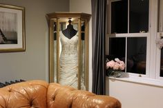 a wedding dress hanging on a hanger next to a window with flowers in it