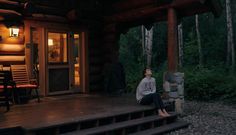 a woman is sitting on the porch of a log cabin at night with her eyes closed