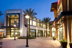 an empty shopping center at night with palm trees in the foreground and lights on