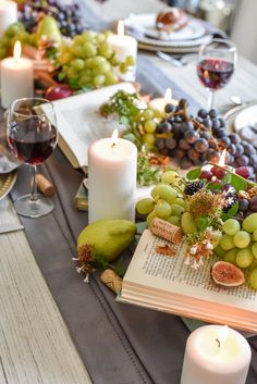 an open book on a table with grapes, pears and candles