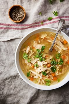 a white bowl filled with chicken and carrots next to a spoon on top of a table