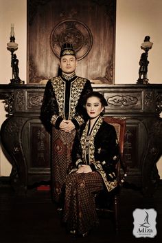 a man and woman sitting next to each other in front of a fireplace