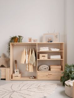 a white rug and some wooden shelves with clothes on them in a room next to a potted plant