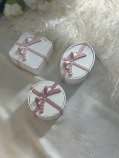 two small round boxes with pink bows on them sitting on a white blanket next to flowers