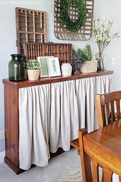 a wooden table topped with vases and plants next to a wall hanging on the wall