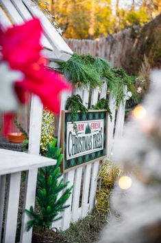 a christmas sign is hanging on a white picket fence with greenery and lights around it