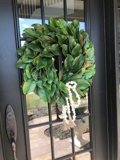 a green wreath on the front door of a house with white beads hanging from it