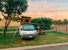 a van parked next to a tree with a person sitting on the ground in front of it