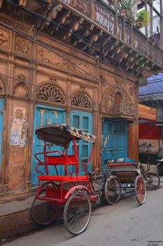 two red rickshaws are parked in front of an old building with blue doors