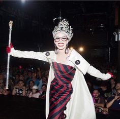 a woman dressed in costume and holding a stick with her arms spread out while people watch