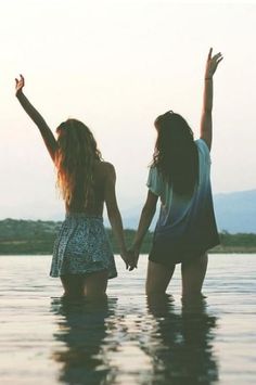 two young women are standing in the water holding hands and looking up at the sky