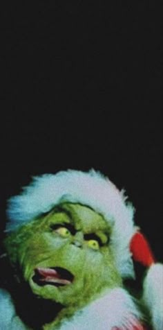 the grinch is wearing a santa hat and holding his hand up to his head