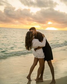 a man and woman kissing on the beach at sunset, with clouds in the background