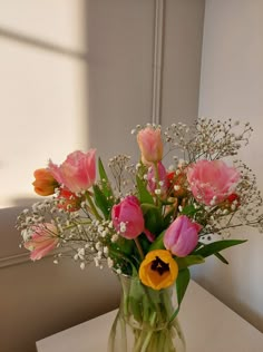 a vase filled with pink and yellow flowers on top of a white table next to a window