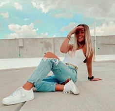 a woman is sitting on the ground with her legs crossed and wearing ripped jeans, white sneakers