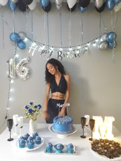 a woman standing in front of a table with cake and cupcakes on it