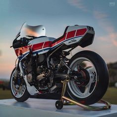 a red, white and blue motorcycle parked on top of a cement block in the sun