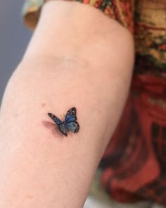 a small blue butterfly tattoo on the right arm and left arm, sitting on someone's hand