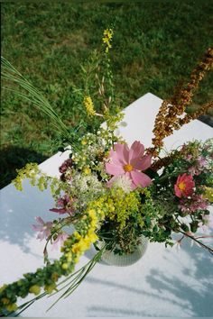 a vase filled with lots of flowers on top of a white tablecloth covered ground