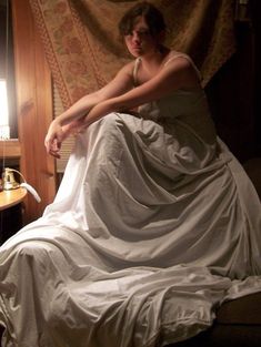 a woman in a white dress sitting on a bed