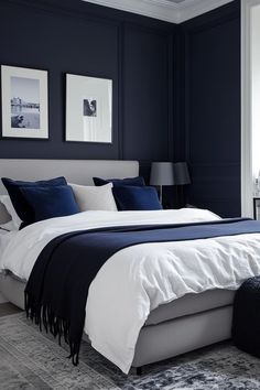 a bedroom with dark blue walls and white bedding is pictured in this image, there are two framed pictures on the wall above the bed