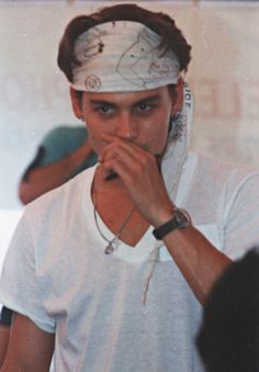 a young man wearing a white shirt and headband holding his hand to his mouth