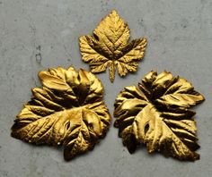 three gold leaf shaped objects sitting on top of a cement floor next to each other