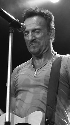 a man holding a guitar while standing next to a microphone on top of a stage