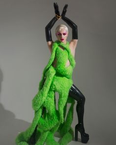 a woman dressed in green and black poses with her legs spread out to the side