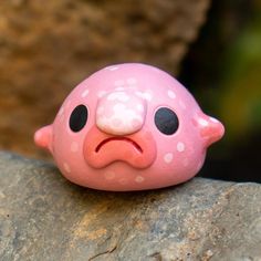 a pink toy with white polka dots on it's face sitting on a rock