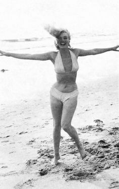 an old photo of a woman in a bathing suit on the beach with her arms outstretched