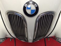 the front end of a white bmw car with chrome grills and emblem on it