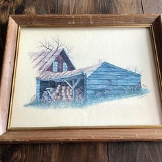 a watercolor painting of a blue barn with logs in the foreground and a wooden frame