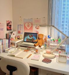 a desk with a computer, books and a teddy bear on it in front of a window