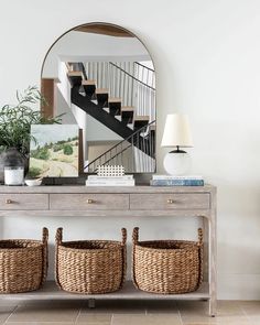 a console table with baskets under it and a mirror above it, next to a staircase