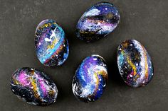 four painted rocks sitting on top of a black surface with colorful paint splattered all over them