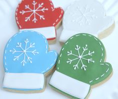 four decorated cookies in the shape of mittens and snowflakes on a white surface