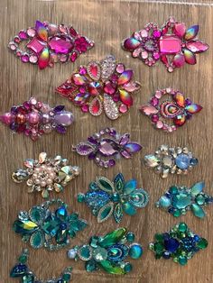 many different colored and shaped brooches on a wooden surface, some with crystals