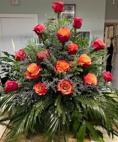 a vase filled with red and orange flowers on top of a wooden table covered in greenery