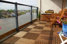 a balcony with chairs and flowers on the floor next to a large body of water