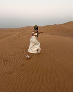 a woman is running in the desert with her arms spread out and she's wearing a white dress