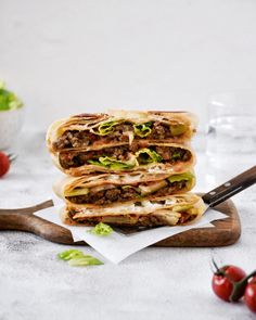 three pita sandwiches stacked on top of each other with lettuce and tomatoes in the background