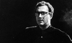 a black and white photo of a man with glasses looking off to the side in front of a dark background