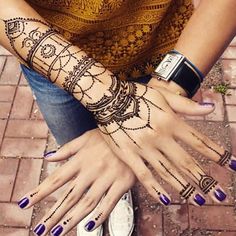 a woman with her hands covered in henna tattoos and purple nail polishes sitting on the ground