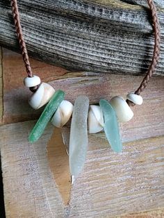 a necklace made with sea glass on a wooden board next to a piece of driftwood