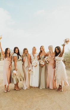 a group of women standing next to each other in front of a dirt field holding bouquets